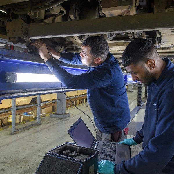 Monteurs in de werkplaats de Werf meten onder de tram elektra van tram door Monteurs meten elektra tram door in werkplaats