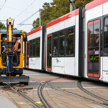 Monteur verwijdert stenen naast het spoor met machine en een rood witte Avenio rijdt langs Monteur verwijdert stenen naast spoor