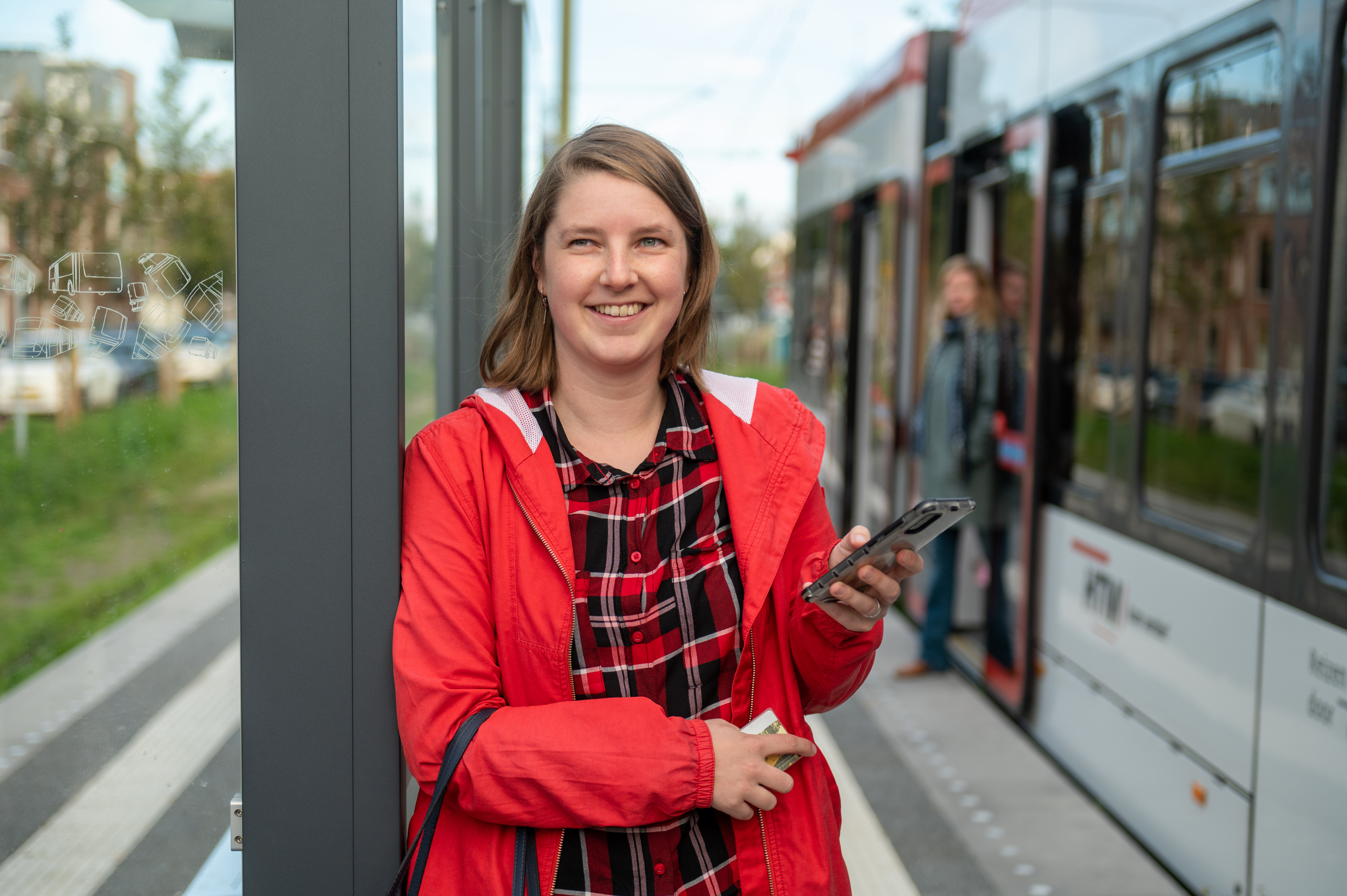 HTM reiziger op tramhalte naast HTM tram gebruikt haar telefoon