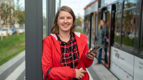 Reiziger op tramhalte HTM reiziger op tramhalte naast HTM tram gebruikt haar telefoon