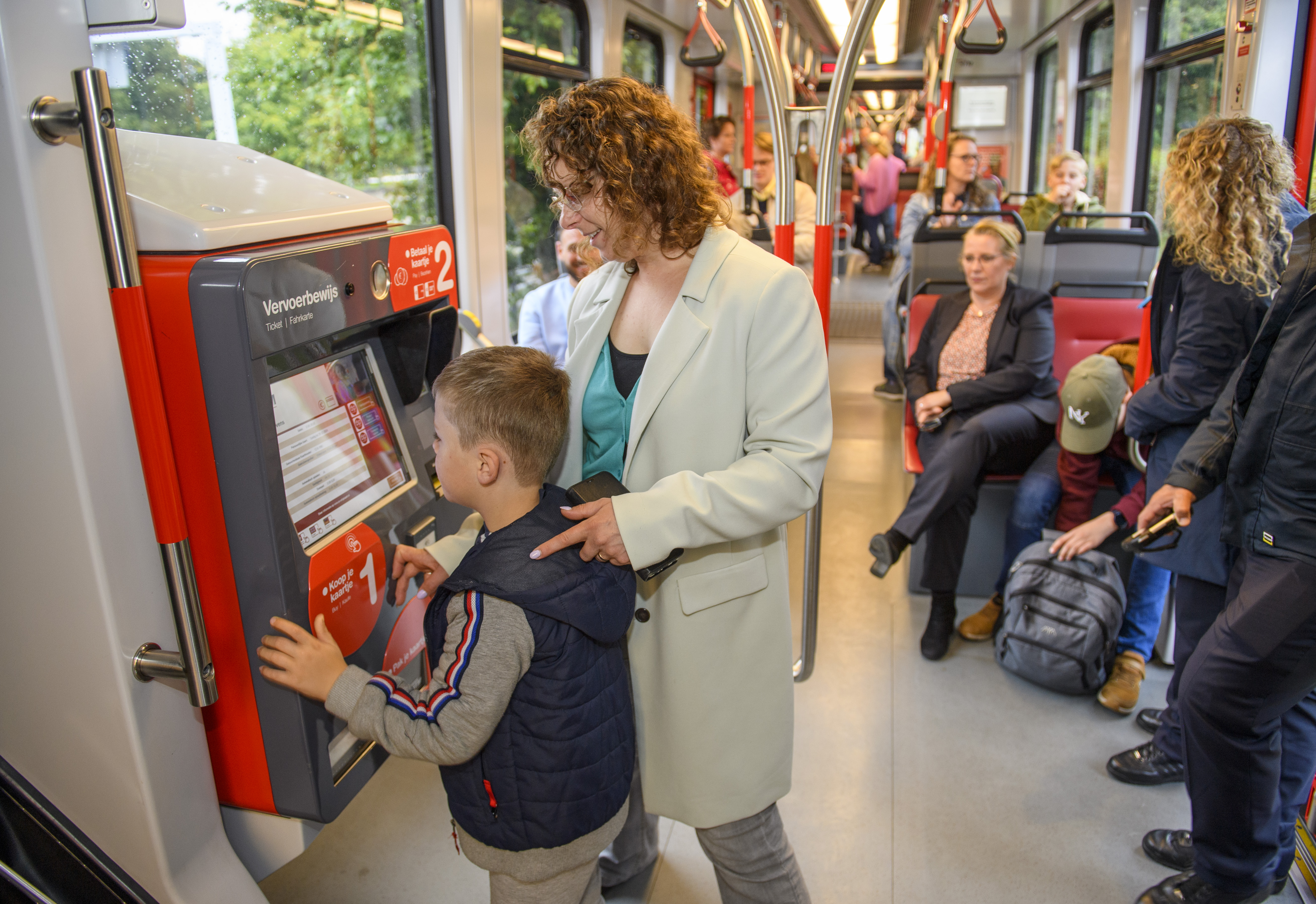 Moeder en kind kopen tramkaartje bij kaartverkoopautomaat in HTM tram
