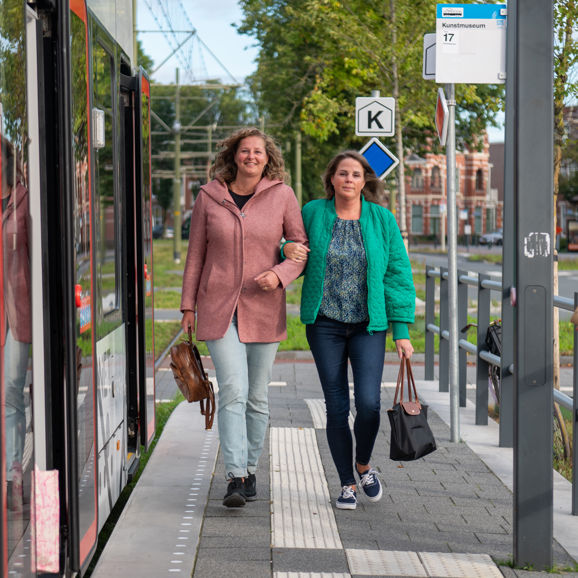 Reizigers lopen op tramhalte Reizigers lopen op halte naast HTM tram en kijken naar de camera