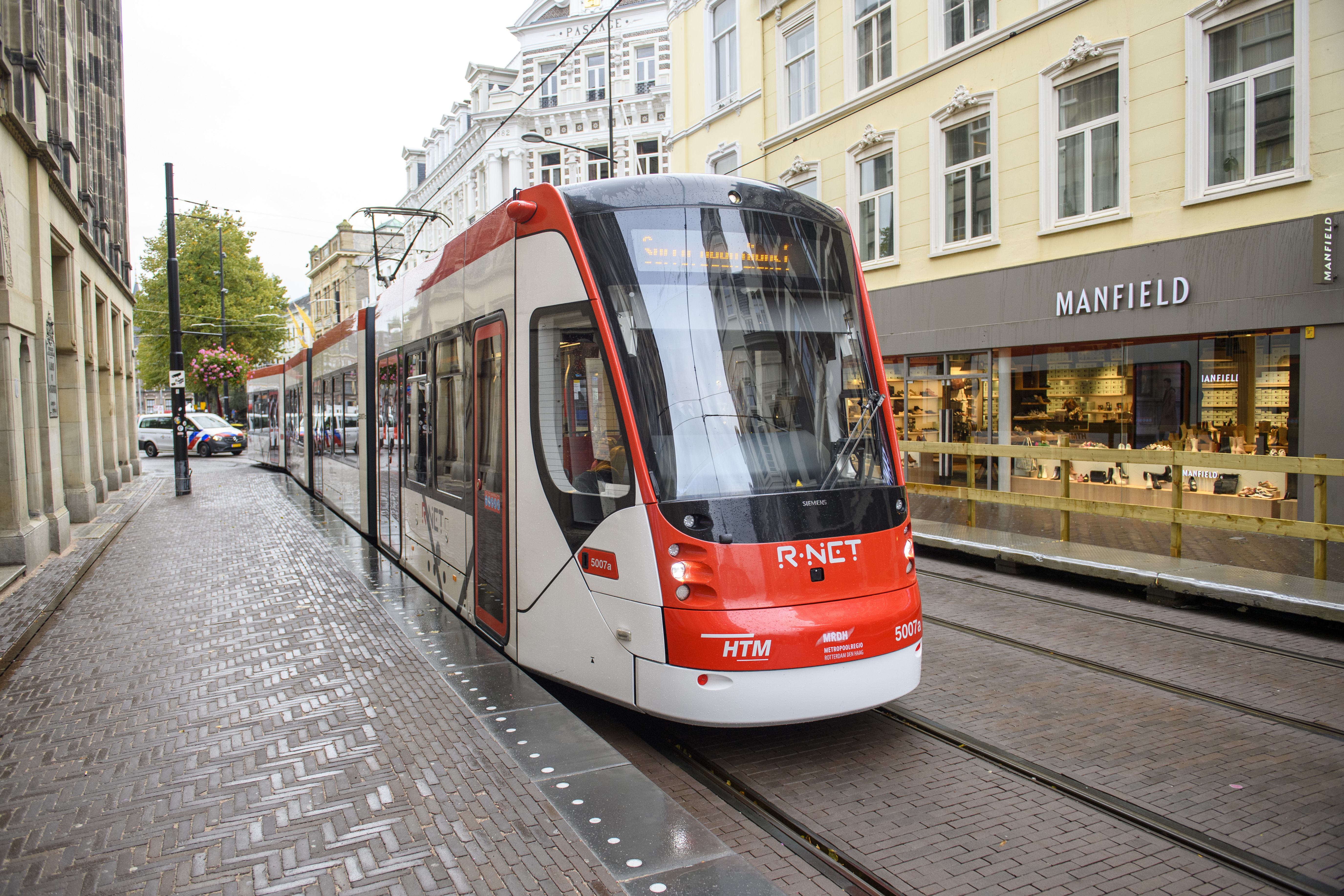 Wit met rode HTM tram rijdt langs winkels in Den Haag