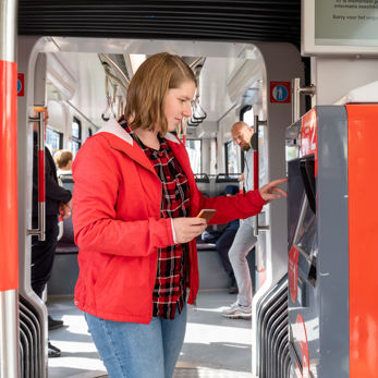 Vrouw koopt kaartje bij kaartverkoopautomaat Vrouw koopt kaartje bij HTM kaartverkoopautomaat in HTM tram