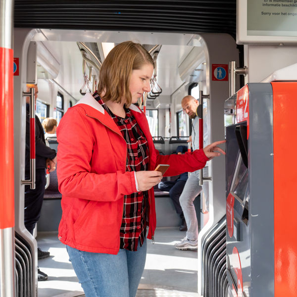 Vrouw koopt kaartje bij kaartverkoopautomaat Vrouw koopt kaartje bij HTM kaartverkoopautomaat in HTM tram