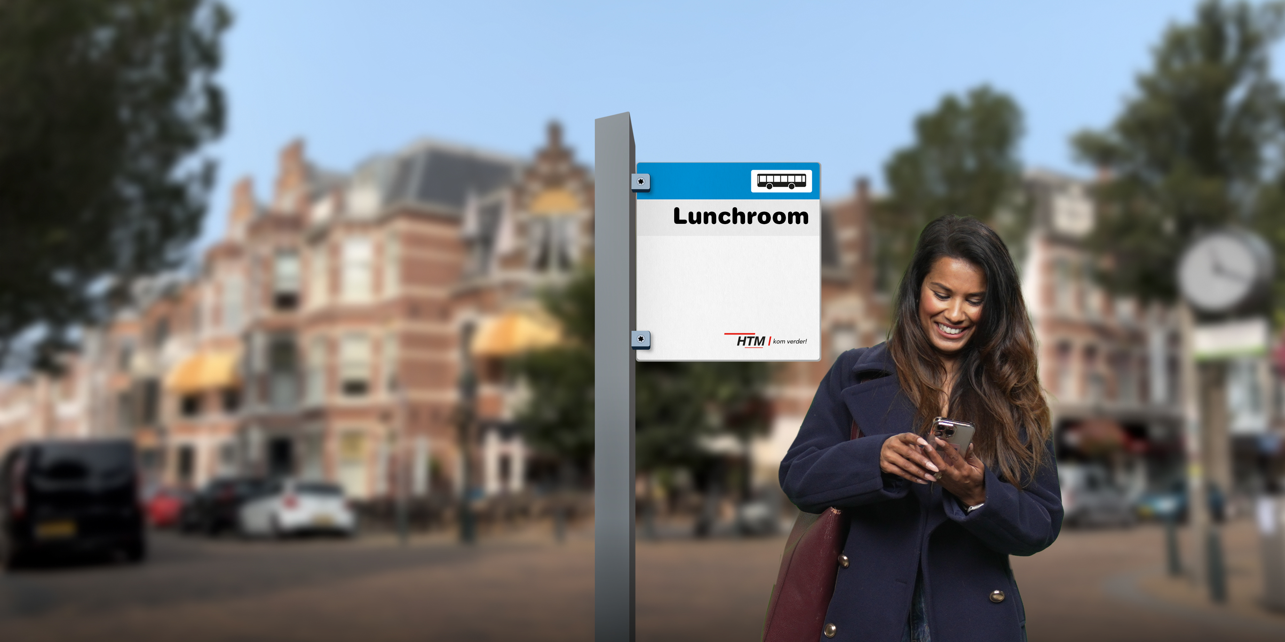 HTM | Zakelijk geklede vrouw staat op een HTM halte en kijkt naar haar telefoon