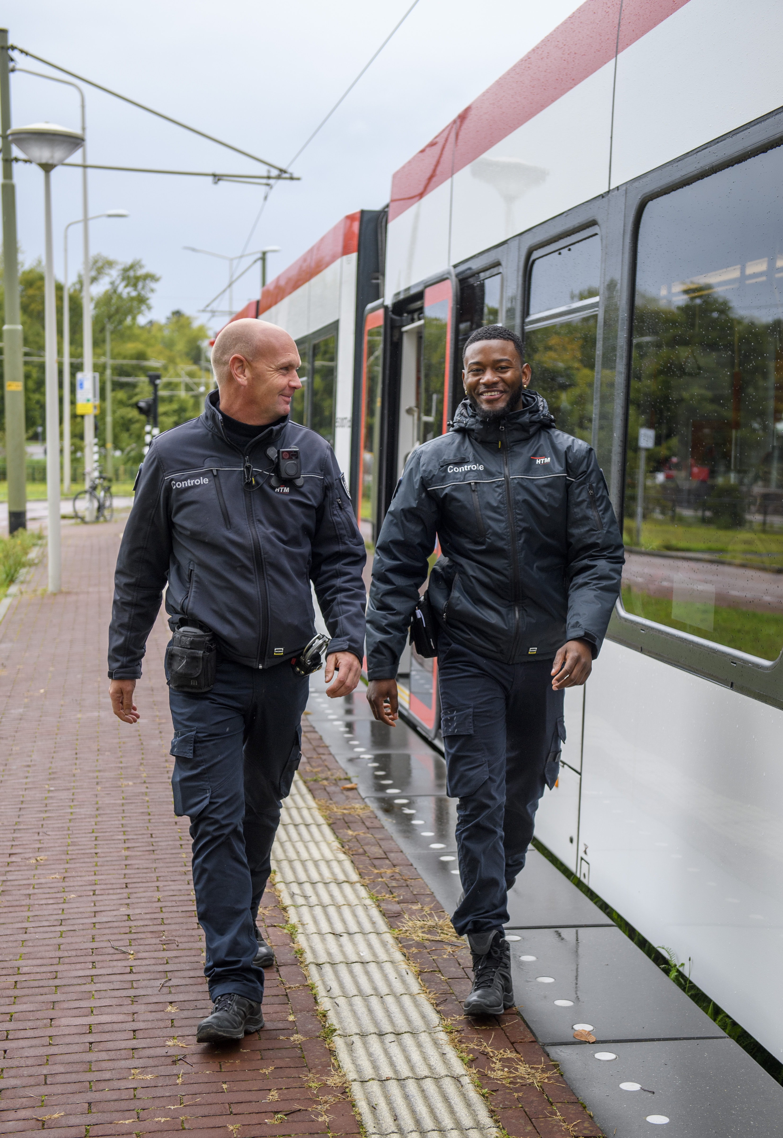 HTM BOA controleurs lopen naast HTM tram en lachen naar de camera