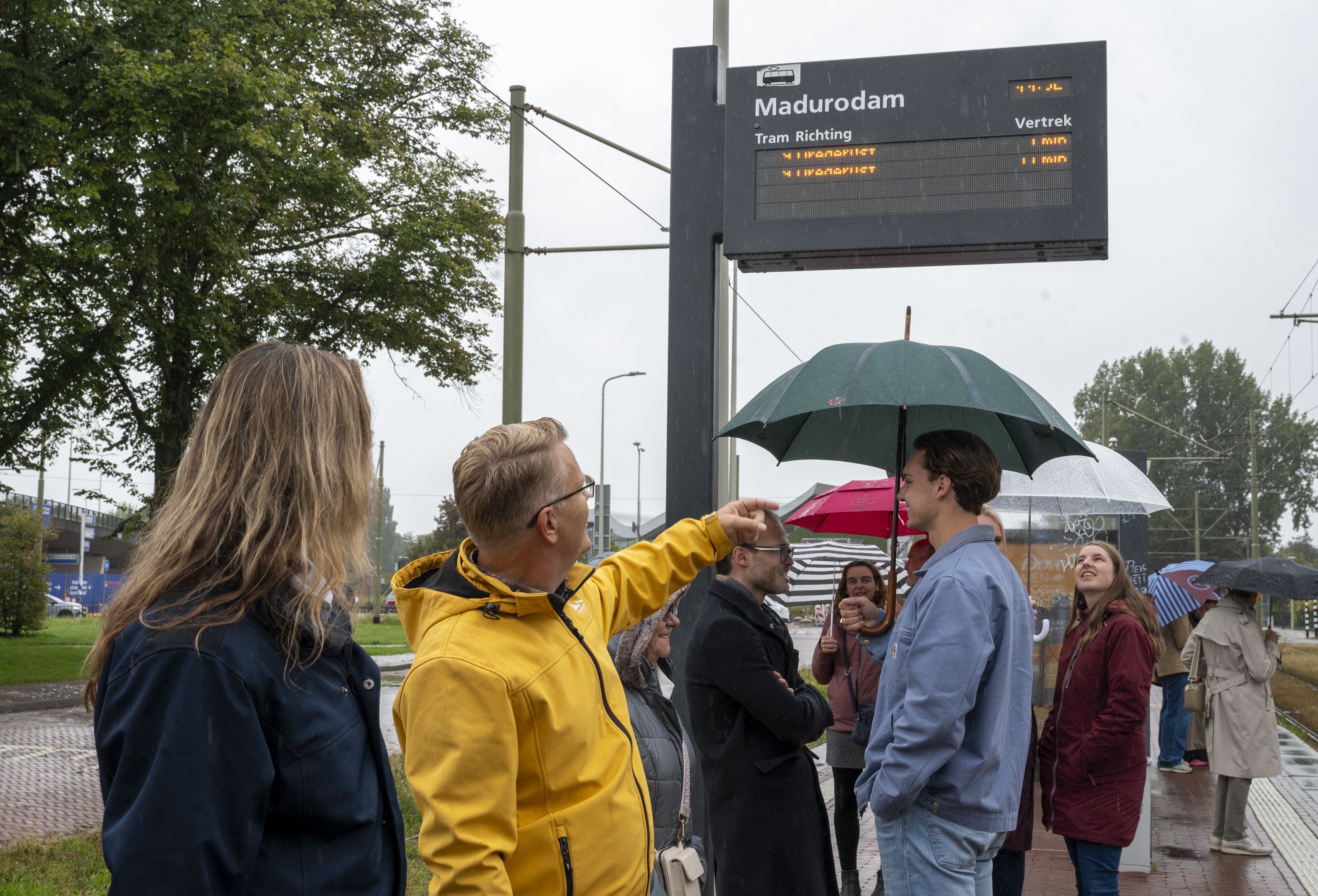 Reizigers op een halte met op de achtergrond een digitaal reisinformatiebord