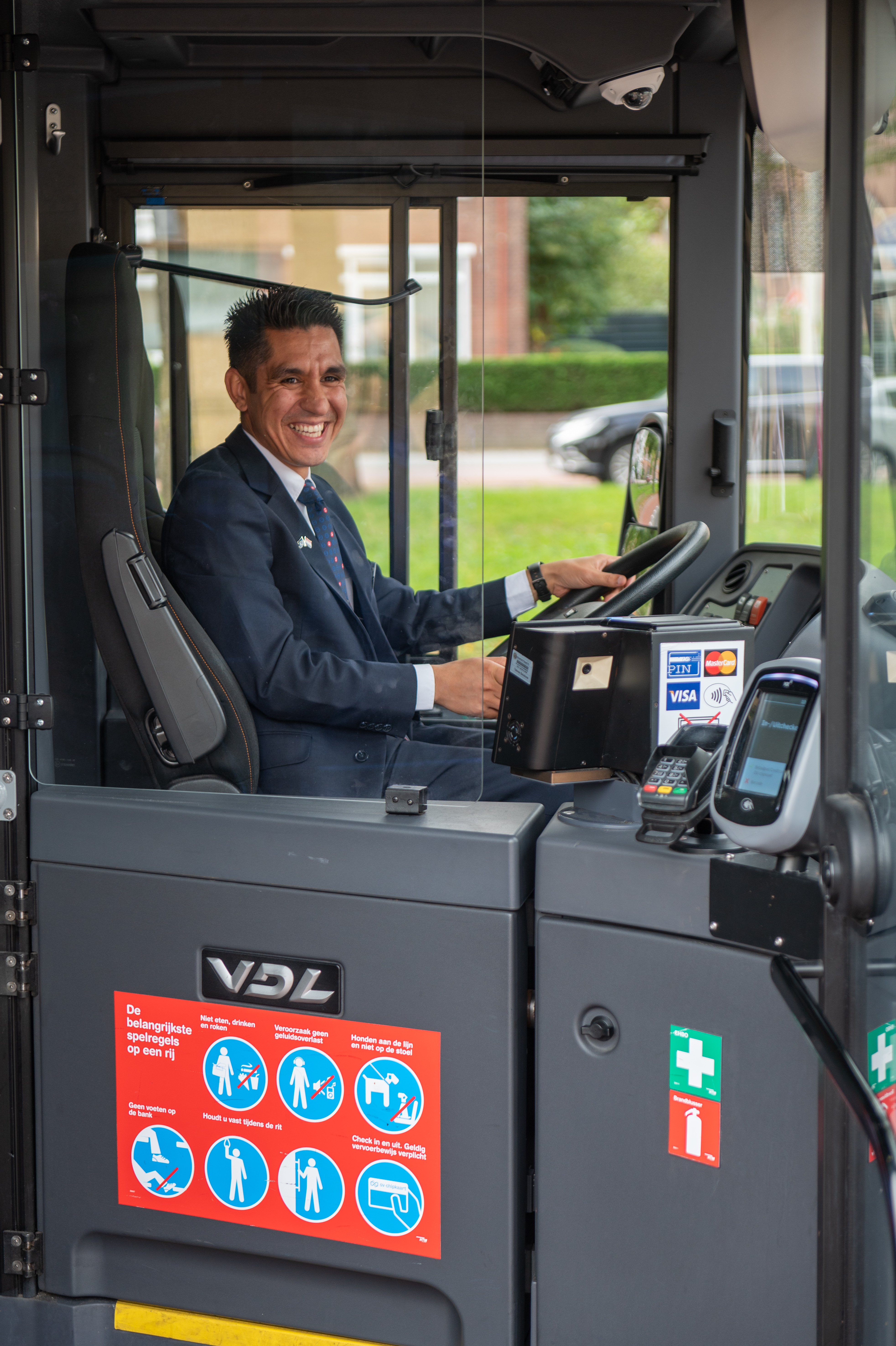 Buschauffeur zit achter het stuur van HTM bus en lacht naar de camera