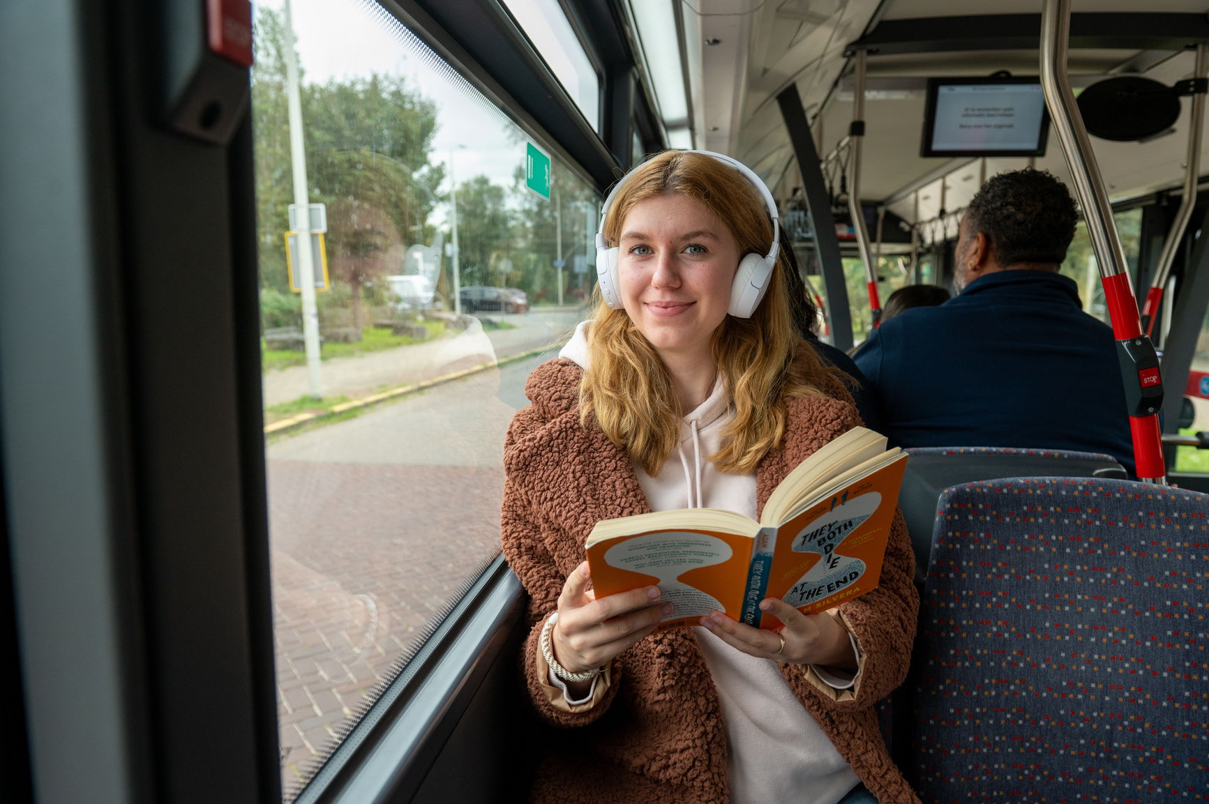Reiziger zit in HTM bus, luistert muziek en leest een boek