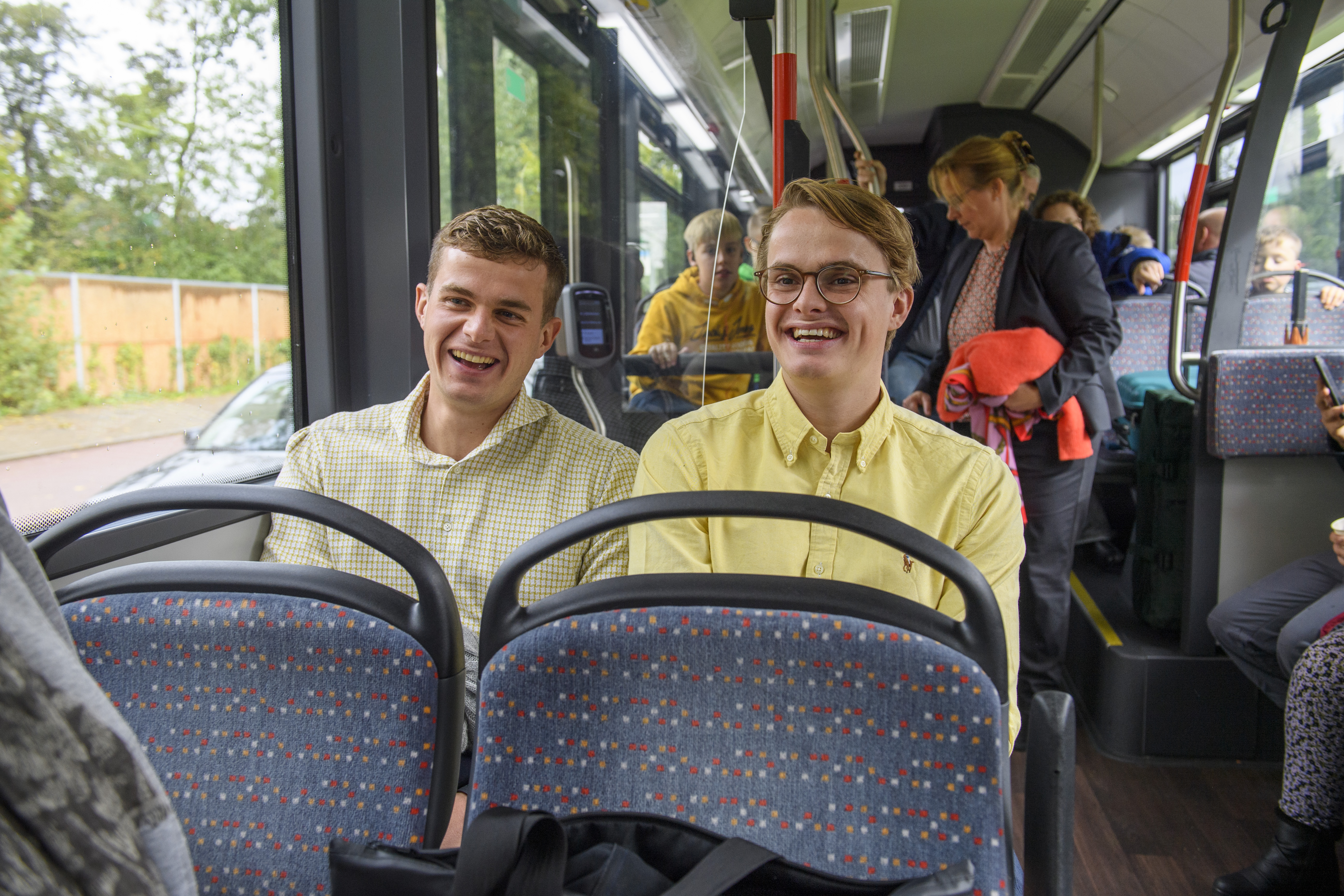 Twee jongens zitten naast elkaar in HTM bus lachen en kijken naar voren