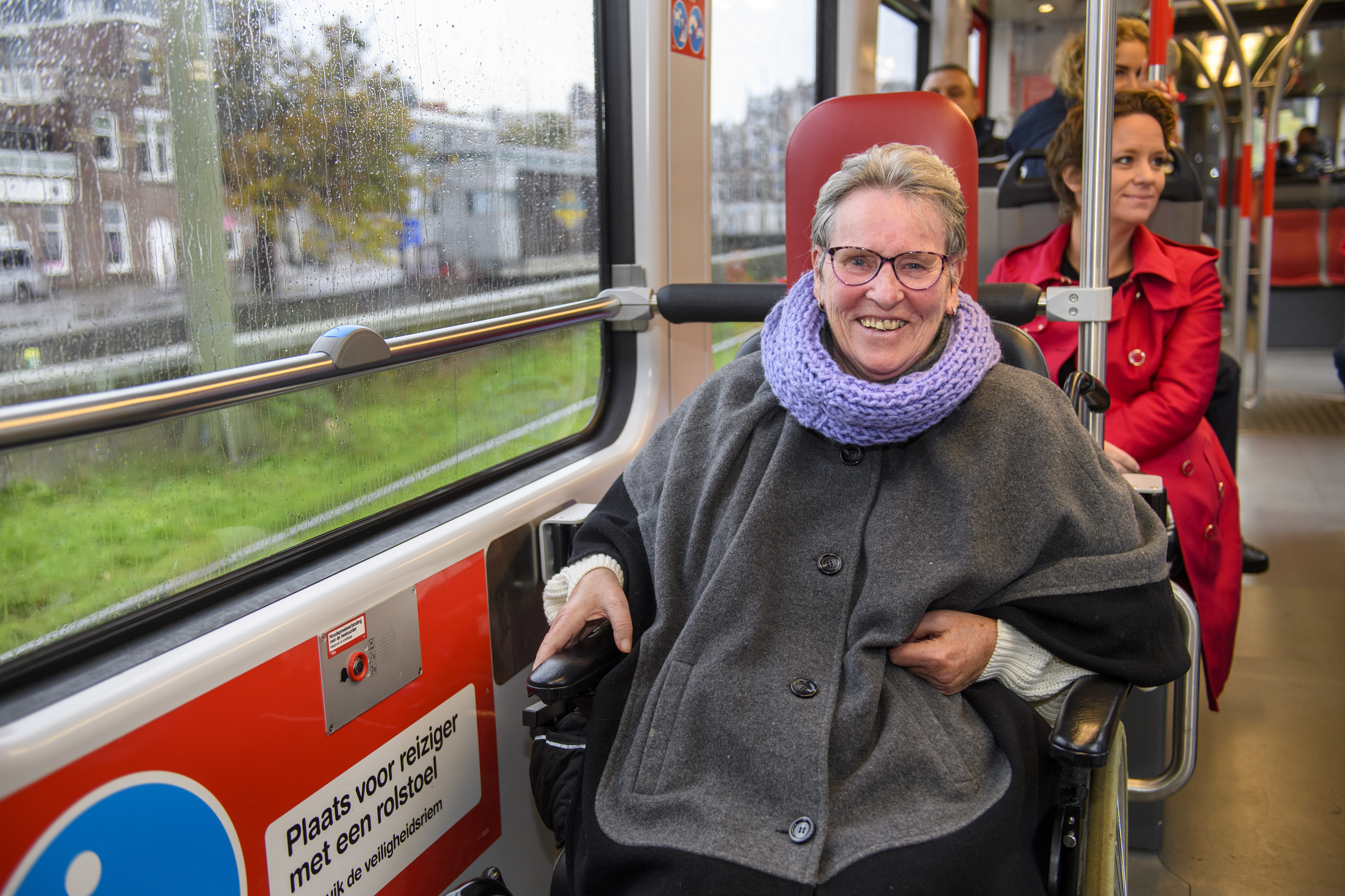 Reiziger in een rolstoel zit in HTM tram en lacht naar de camera