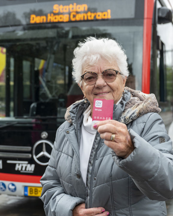 Oude vrouw met bril staat voor een HTM bus met een nieuwe roze OV-pas in haar hand Oude vrouw met bril staat voor een HTM bus met een nieuwe roze OV-pas in haar hand