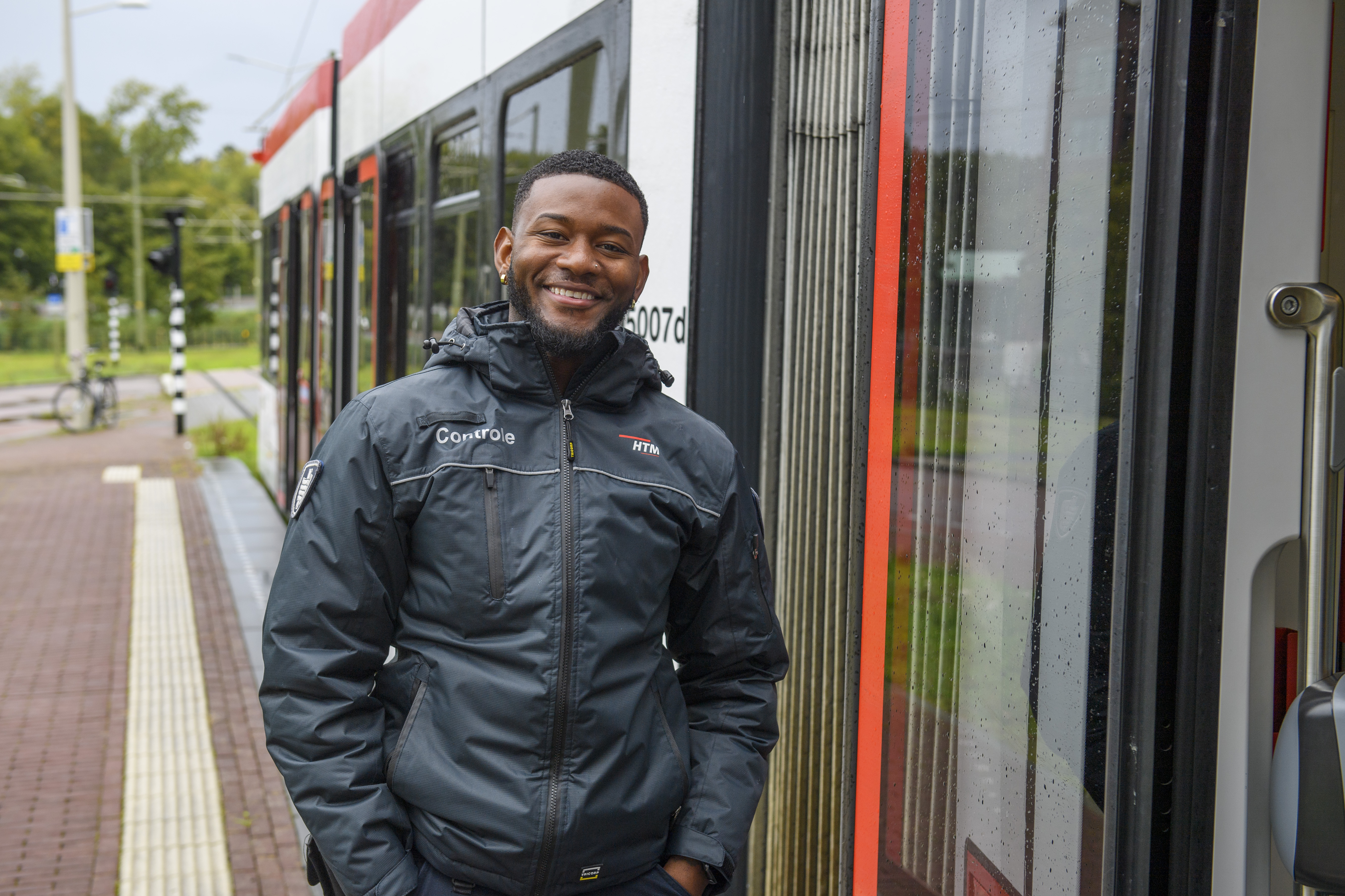 HTM BOA controleur staat naast HTM tram en lacht naar de camera
