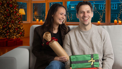 Lachend stel zit samen op de bank voor de kerstboom met kerstcadeautjes in hun handen Lachend stel zit samen op de bank voor de kerstboom met kerstcadeautjes in hun handen