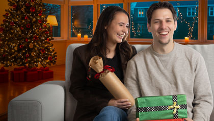 Lachend stel zit samen op de bank voor de kerstboom met kerstcadeautjes in hun handen Lachend stel zit samen op de bank voor de kerstboom met kerstcadeautjes in hun handen